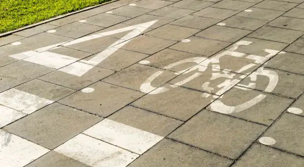 Un carril bici pintado sobre un **damero carretera** de baldosas grises. Una flecha blanca indica la dirección, seguida por el símbolo de una bicicleta.