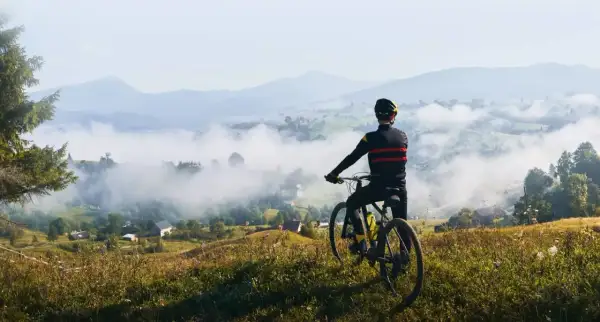 Rowerzysta podziwia mglisty krajobraz dolnośląskiej krainy rowerowej. W oddali góry i malownicze wioski.