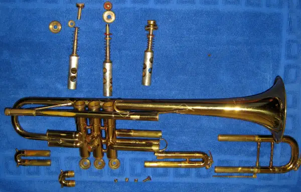 Rozłożona trąbka, instrument dęty blaszany, leży na niebieskim tle. Widać jej poszczególne części: korpus, wentyle, ustnik i inne elementy.