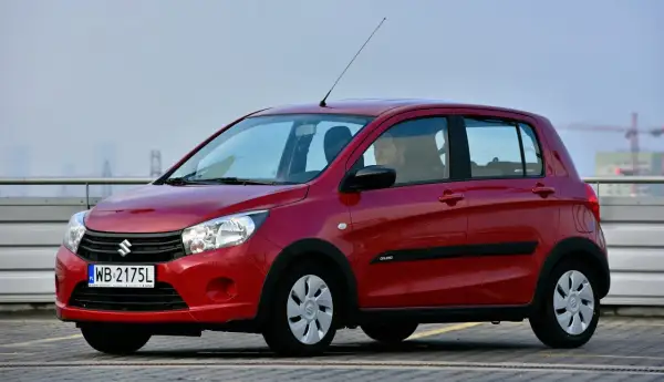 Czerwony Suzuki Celerio z kierowcą za kierownicą, zaparkowany na zewnątrz.