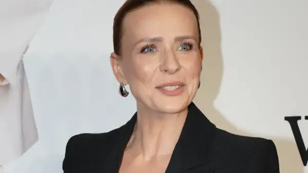 Aneta Zając w czarnej marynarce, z dużymi kolczykami, uśmiecha się. Jej partner, jeśli jest obecny, nie jest widoczny.