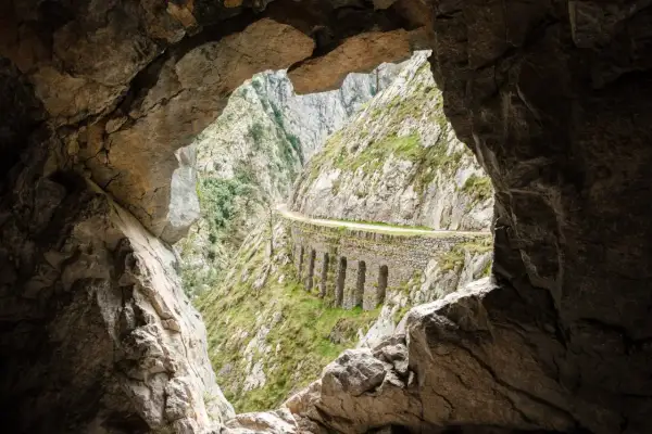 Vista desde una cueva de la ruta del Cares, con un camino tallado en la roca y arcos de piedra.