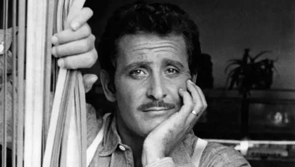 Domenico Modugno, con la mano appoggiata al viso, guarda pensieroso, mentre l'altra mano stringe delle corde.