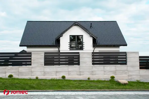 Nowoczesne projektowanie ogrodzenia z betonowych bloczków i czarnych paneli, otaczające biały dom z czarnym dachem.