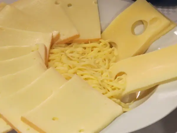 Assiette de fromages variés, dont des tranches d'Emmental avec ses trous caractéristiques, et du Gruyère râpé. La différence entre gruyère et emmental est subtile.