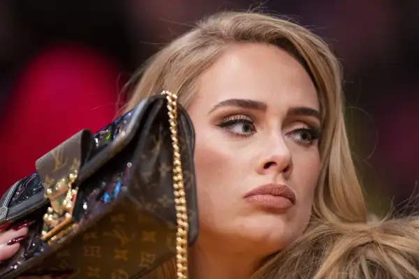 Adele z torebką na koncercie, zamyślona, z makijażem i blond włosami.