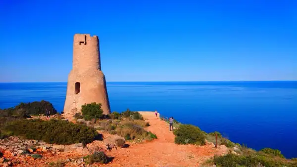 Torre defensiva en la costa, un lugar ideal que ver en Gata, con el mar azul de fondo y visitantes disfrutando del paisaje.