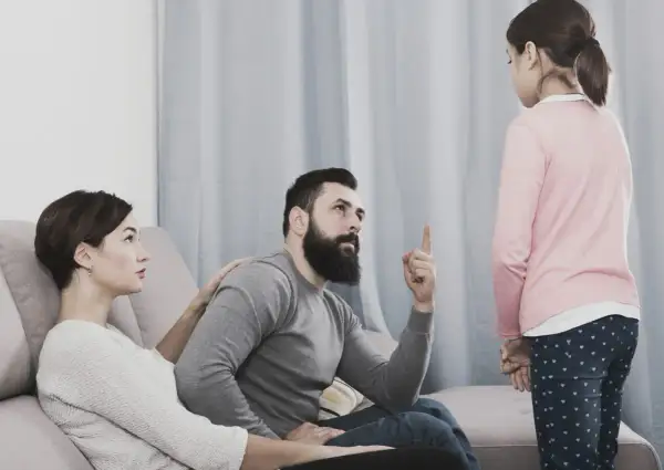 Una bambina ascolta il padre che la ammonisce, mentre la madre, con un'espressione preoccupata, le appoggia una mano sulla spalla, forse per alleviare la sua paura di perdere i genitori.