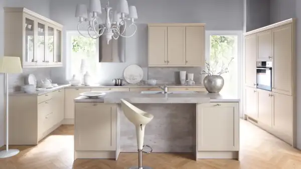 Jasna kuchnia shabby chic z kremowymi meblami, kamiennym blatem i eleganckim żyrandolem.