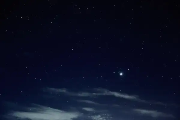 Nocne niebo pełne gwiazd, z widocznymi chmurami i dwoma jasnymi punktami, być może planetami.