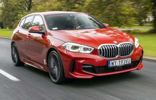 Czerwone BMW F40 pędzi po drodze, otoczone zielenią drzew.