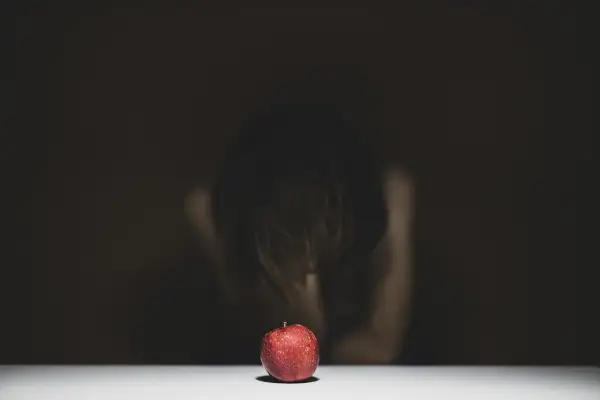 Czerwone jabłko na białym tle, w tle niewyraźna postać pochylona nad nim.