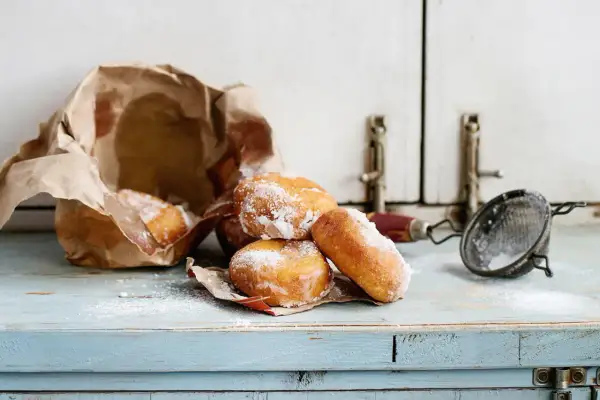 Pączki posypane cukrem pudrem, częściowo w papierowej torbie. Wskazówki, jak przechowywać pączki, by były świeże.