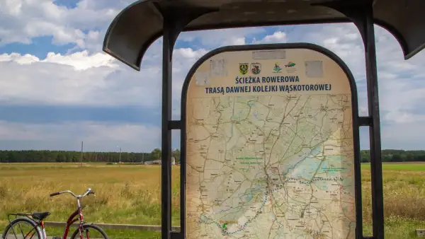 Mapa informuje o ścieżce rowerowej trasą dawnej kolejki wąskotorowej. Obok stoi rower.