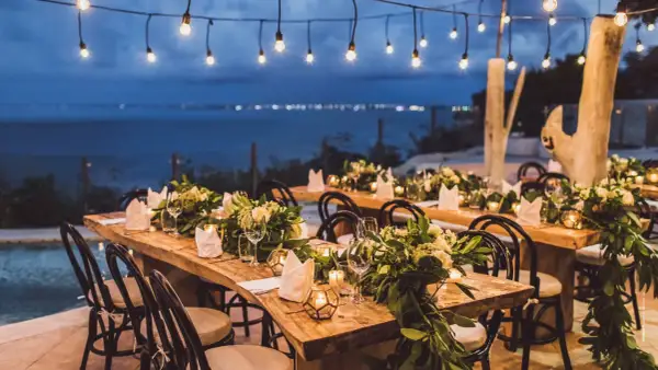 Tavoli apparecchiati per un magico matrimonio di sera, con luci soffuse e vista sul mare.