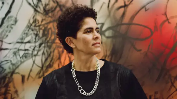 A striking portrait of artist Julie Mehretu, her gaze thoughtful, set against a vibrant, abstract background that echoes her dynamic style.