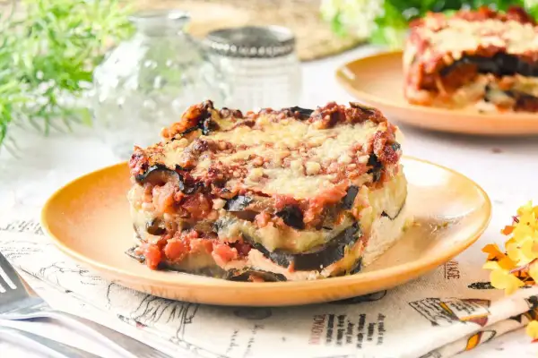 Porción de lasaña de berenjena horneada, con capas de berenjena, salsa de tomate y queso derretido, servida en un plato naranja.