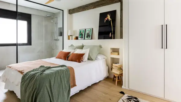 Dormitorio con ducha integrada, cama con mantas cálidas y cuadros. Una reforma sin obras que transforma el espacio con estilo y funcionalidad.