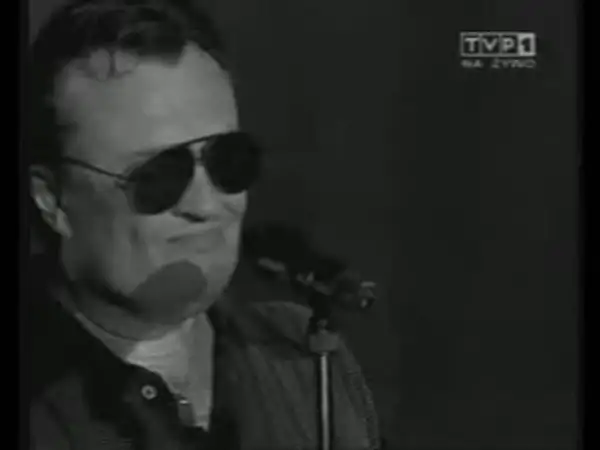 Mężczyzna w okularach przeciwsłonecznych śpiewa do mikrofonu. Widać logo TVP1. A po nocy przychodzi dzień.