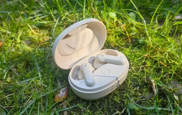 Soundcore P2 Mini Test: Kompakte weiße Ohrhörer in ihrer Ladeschale, umgeben von grünem Gras und Morgentau.