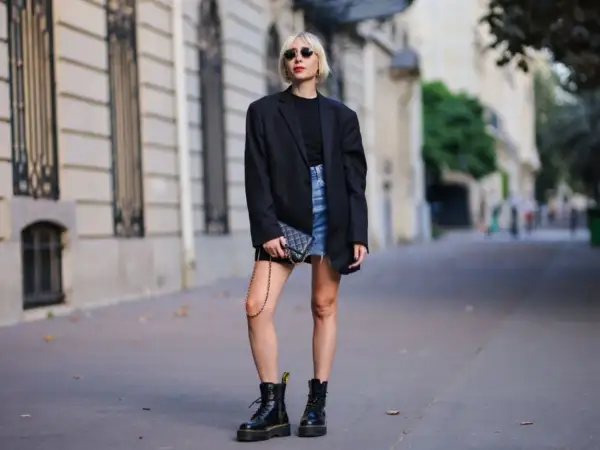 Kobieta w czarnym blazerze i jeansowej spódniczce nosi kultowe buty Dr. Martens, które mają bogatą historię.
