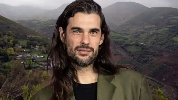 Oliver Laxe, director, posa con una barba cuidada y pelo largo, frente a un paisaje montañoso de Galicia.