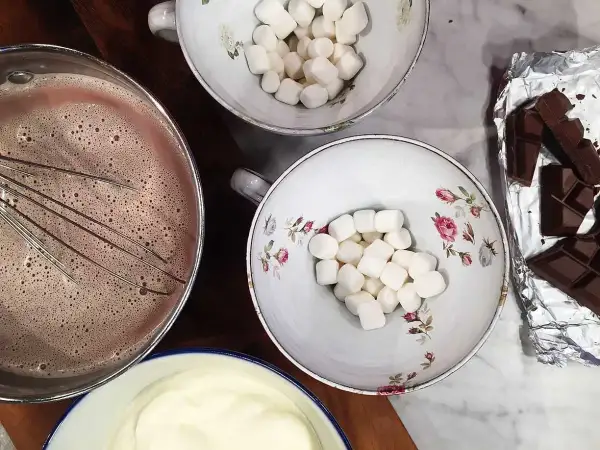 Förberedelser för en mysig stund med varm choklad. Vispad choklad i kastrull, marshmallows i skålar och chokladkakor redo att smältas.