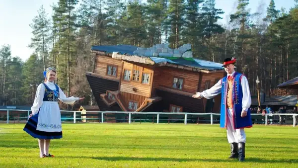 Para z ludźmi w strojach ludowych zaprasza do Domu do Góry Nogami, jednej z głównych atrakcji dla dzieci w Szymbarku.