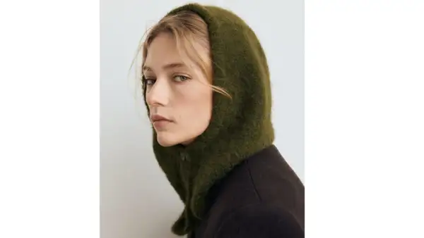 Mujer con un balaclava verde de lana, cubriendo su cabeza y cuello, con un abrigo oscuro.