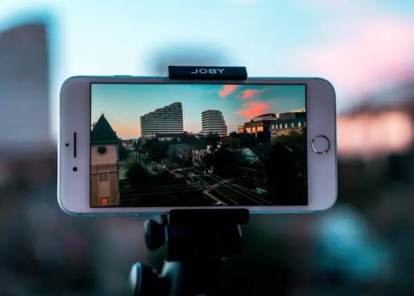 iPhone nagrywa timelapse miasta o zachodzie słońca. Widać budynki, drzewa i ulicę.