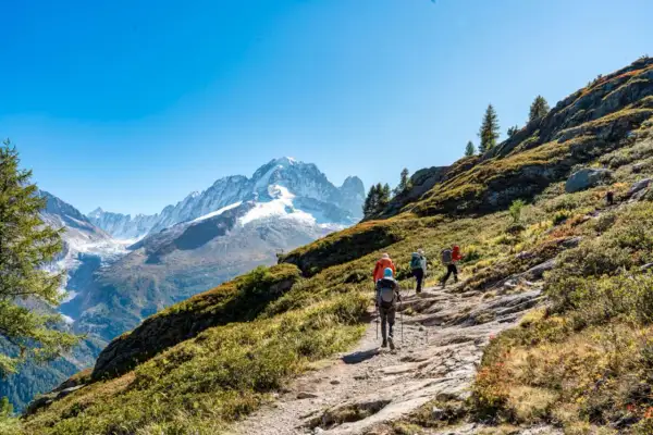 Senderismo en Francia, un grupo de excursionistas asciende por un sendero rocoso con vistas a picos nevados y un glaciar.