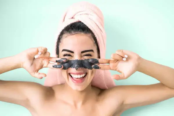 Ragazza felice con maschera viso nera, si chiede quante volte a settimana usarla per una pelle radiosa.