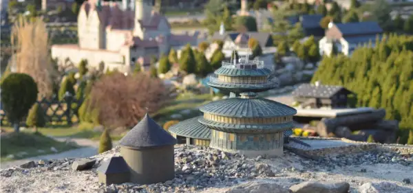 Miniaturowe budowle, w tym okrągły budynek z kopułą i wielopoziomowa konstrukcja, tworzą krajobraz jednego z parków miniatur w Polsce.