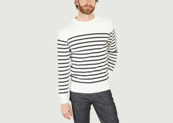 Un homme porte un pull marinière marin à rayures bleues et blanches, avec un jean brut.