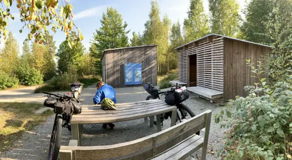Cykelturist vilar vid rastplats i Åsnen nationalpark. Två packade cyklar står vid ett bord och bänkar.