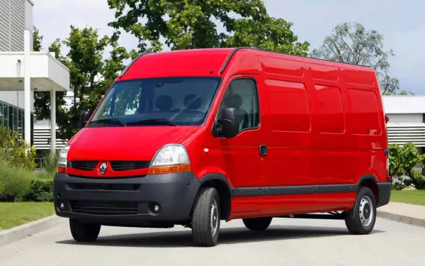 Czerwony Renault Master 2, gotowy do pracy, stoi na tle zieleni i nowoczesnego budynku.