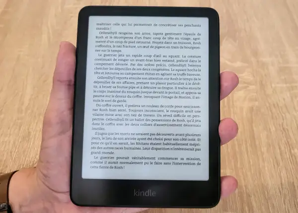 Main tenant un appareil Kindle format e-reader, affichant un texte en français sur fond noir.