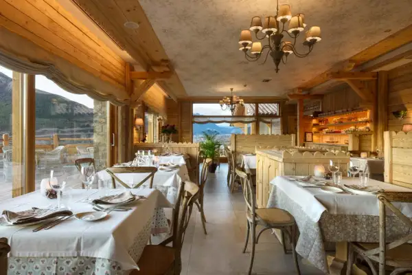 Elegante comedor de madera con mesas puestas, vistas a la montaña. Un lugar perfecto para disfrutar de los restaurantes del Valle de Tena.