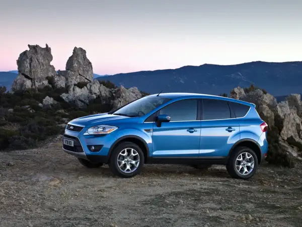 Niebieski Ford Kuga MK1 na tle skalistego krajobrazu o zachodzie słońca.