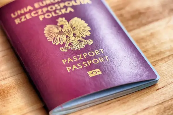 Ciemnoczerwony paszport biometryczny Rzeczypospolitej Polskiej z godłem i napisem "PASZPORT PASSPORT" na drewnianym tle.