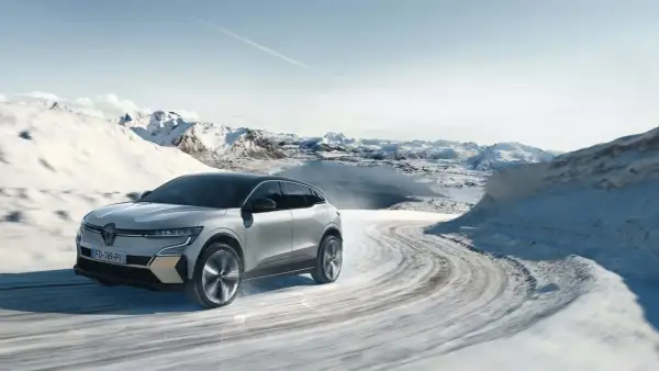 Voiture électrique avec pompe à chaleur traversant un paysage hivernal enneigé, montagnes et lac gelé en arrière-plan.
