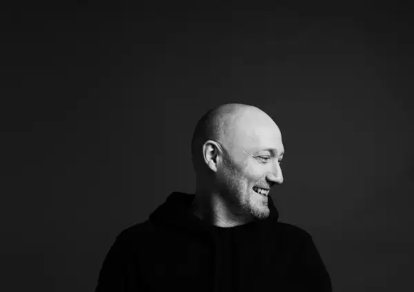 Uśmiechnięty Paul Kalkbrenner w czarnej bluzie, gotowy na koncert w Warszawie.