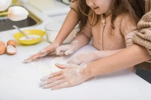 Radość z zabawy w domu z 3 latkiem. Dziecko i mama wspólnie zagniatają ciasto, ubrudzone mąką.