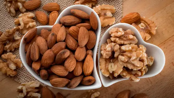 Deux bols en forme de cœur remplis d'amandes et de noix. Une belle présentation de ces oléagineux, parfaits pour une liste d'en-cas sains.