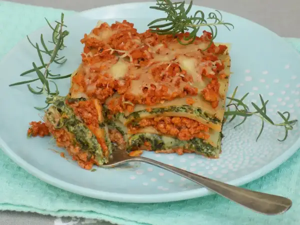 Pyszny przepis na lasagne z mięsem mielonym i szpinakiem, podana na talerzu z gałązkami rozmarynu.