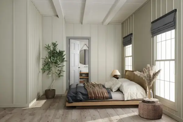 Letto in legno con coperte, posizionato di fianco alla porta aperta che conduce al bagno. Pianta in vaso e finestra con luce naturale.