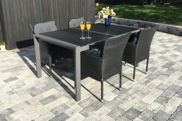 En vacker stenlagd uteplats med ett mörkt matbord och stolar, perfekt för inspiration. Två glas med apelsinjuice står redo.