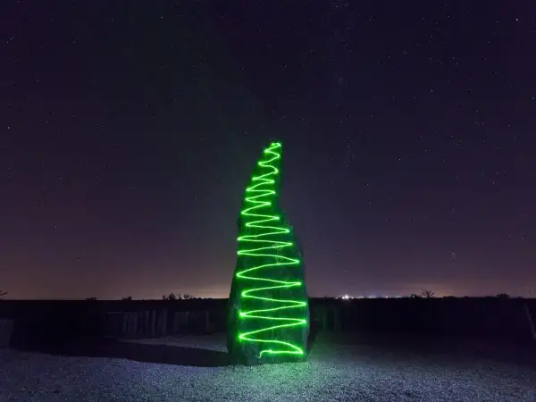 Menhir illuminato da una spirale di vernice elettroluminescente verde sotto un cielo stellato.