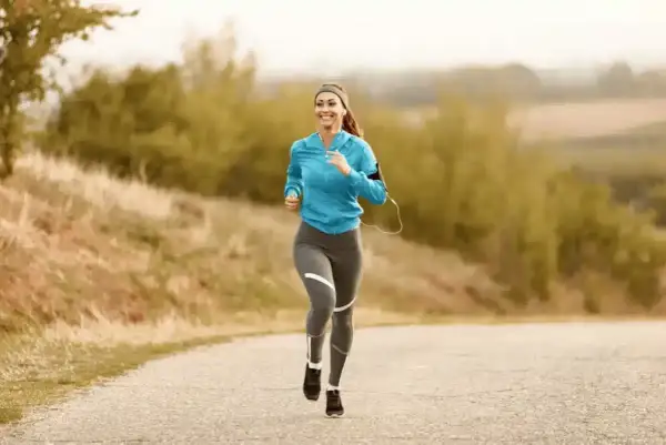 Femme souriante courant sur une route de campagne, musique dans les oreilles, pour un sport à 180 bpm.