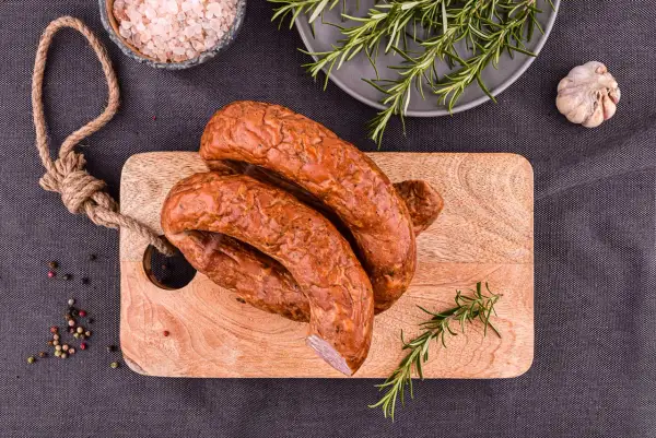Wędzona kiełbasa na desce z rozmarynem, solą i pieprzem.